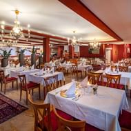 Elegant restaurant with white-clothed tables, wooden chairs with red upholstery, chandeliers, and red walls with wooden beams.