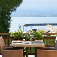 Restaurantterrasse im Hotel La Barcarolle in Prangins mit Korbstühlen, gedecktem Tisch mit Blumen und Blick auf Genfer See und Steg.