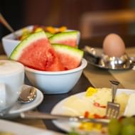 Frühstückstisch mit Wassermelonenscheiben, Käseplatte, gekochtem Ei, Kaffeetasse und Obstschale im Hotel Villa Geyerswoerth in Bamberg.