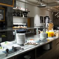 Frühstücksbuffet im Hotel Continental Park in Luzern mit gestapelten Tellern, Saftspender und Speisen auf Marmortheke in modernem Speiseraum.