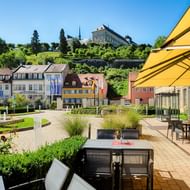 Hotelterrasse mit gelben Sonnenschirmen und Tischen mit Blick auf Bambergs historischen Stadtplatz und Schloss auf dem Hügel.