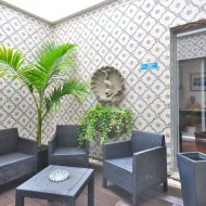 Outdoor terrace at Porto Domus Hotel with dark wicker furniture, palm plants, and decorative Portuguese tiles on walls with shell ornament.