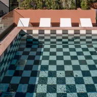 Artcore Hotel Porto pool with black and white checkered tiles. White sun loungers line the terrace, surrounded by greenery.