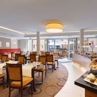 Modern breakfast room at Best Western Bamberg with tables, chairs, buffet station, and terrace access. Warm lighting and neutral decor.