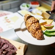 Frühstücksauswahl mit Körnerbrötchen, Käsescheiben, Gurke, Tomate und Aufschnitt auf weißen Tellern im Hotel Continental Park, Luzern.