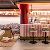 Modern bar at Artcore Hotel Porto with red column, striped counter, bar stools, decorative tile wall, and white curved seating area.