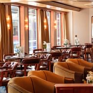 Elegant MS Swiss Crown lounge with golden curtains, round tables, brown leather chairs, and white orchids by large windows.