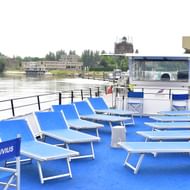 MS Fluvius sun deck with blue loungers Sun deck of MS Fluvius river cruise ship with rows of blue deck chairs and loungers. River and buildings visible in background.