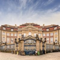 Historic Erbdrostenhof palace in Münster with baroque facade, ornate entrance gate, and cobblestone courtyard under blue sky with clouds.