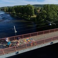 Luftaufnahme von Radfahrern mit Rädern auf einer Brücke über die Saar. Bunte Straßenkunst ist auf dem Brückengehweg sichtbar.