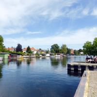 Waterfront promenade in Malchow with calm lake, wooden pier, colorful houses, green trees and blue cloudy sky.