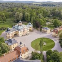 Luftaufnahme von Schloss Belvedere in Weimar mit barocken gelben Gebäuden, rundem Rasen und umgebender Parklandschaft in Thüringen.