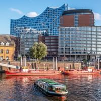 Hamburger Hafen mit Booten auf der Elbe und der markanten gläsernen Elbphilharmonie, die über historischen Backsteingebäuden aufragt.