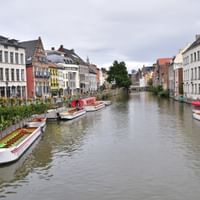 Kanal in Gent gesäumt von bunten historischen Gebäuden und Ausflugsbooten. Traditionelle flämische Architektur mit weißen, gelben und roten Fassaden.
