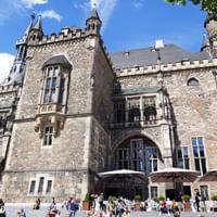 Aachener Rathaus, ein mittelalterliches gotisches Gebäude mit Steinmauern, spitzen Türmen und verzierten Fenstern. Besucher versammeln sich auf dem Platz.