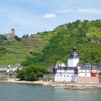Burg Pfalzgrafenstein auf einer kleinen Insel im Rhein mit der Stadt Kaub und terrassierten Weinbergen an den Hängen im Hintergrund.