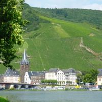 Historic town of Bernkastel-Kues along the Moselle River with traditional buildings, church spires, and steep vineyard slopes rising behind.