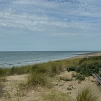 Wooden bench on sandy dunes with beach grass overlooking a calm beach and sea in Zeeland. The sky is partly cloudy.