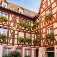Traditional German half-timbered buildings forming a courtyard in Mainz with red timber frames, flower boxes, and a sign reading 'Wilden Hans'.