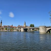 Stone bridge crossing the Main River in Kitzingen with historic town buildings and church towers visible along the waterfront under blue sky.