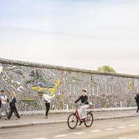 Radfahrer fährt an der bunten East Side Gallery der Berliner Mauer vorbei. Die Betonmauer zeigt kunstvolle Straßenkunst mit wirbelnden Mustern.