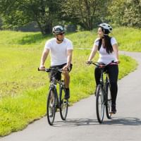 Two cyclists with helmets riding bikes on paved path through green countryside near Marburg on the Lahn Cycle Route.