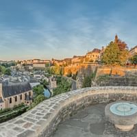 Circular stone platform of Monument du Millénaire with compass rose, overlooking Luxembourg's old town with church spire and fortifications.