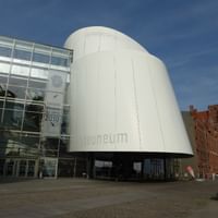 Modern white curved building of the Ozeaneum in Stralsund with glass facade and historic red brick buildings in background under blue sky.