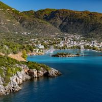 Küstenbucht auf dem Peloponnes, Griechenland Malerische Bucht auf dem Peloponnes mit türkisfarbenem Wasser, weißen Gebäuden entlang der Küste, felsiger Küstenlinie und grünen Bergen.