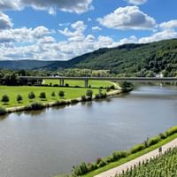 Saar River valley near Saarburg with bridge Scenic view of the Saar River near Saarburg with a concrete bridge crossing the water, surrounded by green hills and vineyards.
