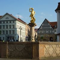 Goldene St. Georg Statue auf Steinsäule auf dem Eisenacher Marktplatz, umgeben von historischen Gebäuden mit Fachwerkhäusern und Kirche.