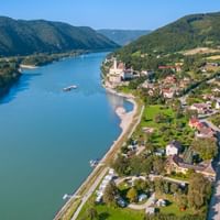 Luftaufnahme von Schönbühel in der Wachau mit Burgruine am Hang, Donau und bewaldeten Bergen in Österreich.