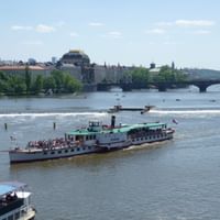 Paddle steamer on Vltava River in Prague White paddle steamer with passengers cruising on the Vltava River in Prague. Historic bridge and baroque buildings visible in background.