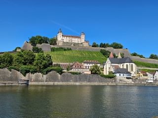 Festung Marienberg auf einem Hügel mit terrassierten Weinbergen, historischen Gebäuden und Kirche am Main in Würzburg unter blauem Himmel.