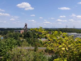 Panoramablick von der Drachenbrücke über das Ruhrgebiet mit grüner Vegetation, Industriegebäuden und einem historischen Hochofenturm.