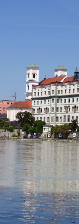 Historische Passauer Altstadt an der Donau mit barocken Kirchtürmen, bunten Gebäuden und mittelalterlichem Turm im ruhigen Wasser.