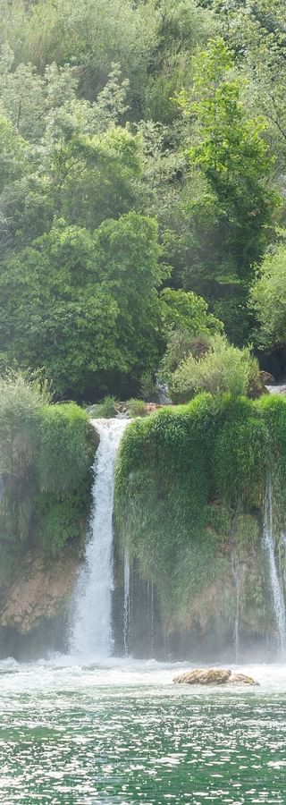 Krka waterfalls in Dalmatia, Croatia Multiple cascading waterfalls at Krka National Park flowing over moss-covered limestone terraces into turquoise pools, surrounded by lush green forest.