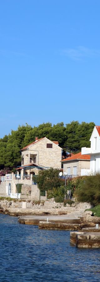 Picturesque coastal village on Solta island with stone houses along the waterfront, a white boat in the bay, and lush green vegetation.
