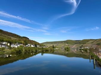 Ruhige Mosel mit Spiegelung des blauen Himmels, Dörfern an beiden Ufern und grünen Weinberghügeln unter klarem Himmel bei Zell und Treis-Karden.
