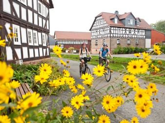 Cyclists in Wetter Amönau village square Two cyclists riding through Wetter Amönau village with yellow flowers in foreground and traditional half-timbered houses in background.
