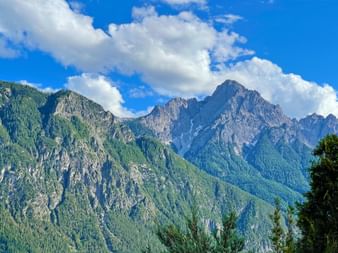 Dramatischer Blick auf die Lienzer Dolomiten mit steilen Felsgipfeln über bewaldeten Hängen unter blauem Himmel mit weißen Wolken.