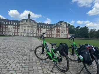 Zwei Tourenräder mit Packtaschen auf Kopfsteinpflaster vor dem barocken Universitätsschloss Münster mit roter Backsteinfassade.
