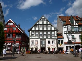Marktplatz in Rintelns Altstadt mit bunten Fachwerkhäusern. Menschen sitzen in Straßencafés unter blauem Himmel mit weißen Wolken.