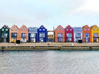 Reihe bunter schmaler Häuser in Stavoren entlang einer Uferpromenade. Die Häuser haben leuchtende Farben wie Orange, Blau, Rot und Gelb.