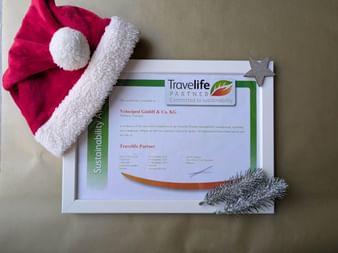 Framed Travelife Partner sustainability certificate for Velociped GmbH with Santa hat and silver star decoration on beige background.