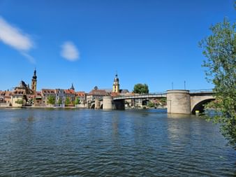 Historische Steinbrücke über den Main in Kitzingen mit Kirchtürmen und bunten Gebäuden entlang des Ufers unter blauem Himmel.