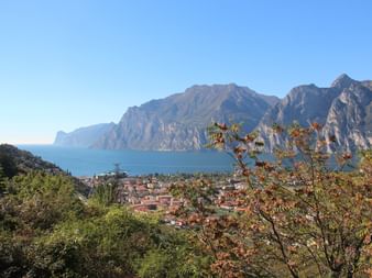 Panoramic view of Lake Garda with Riva del Garda town nestled between dramatic mountains and blue lake waters under clear sky.