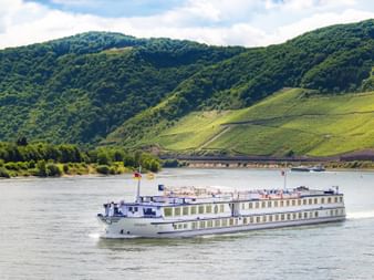 Weißes Passagierschiff MS Olympia fährt auf der Mosel mit terrassierten Weinbergen an grünen Hängen und bewölktem Himmel im Hintergrund.
