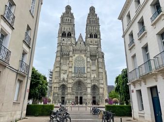 Gotische Kathedrale mit Zwillingstürmen und verzierter Fassade, von der Straße aus betrachtet mit geparkten Fahrrädern und weißen Wohngebäuden.