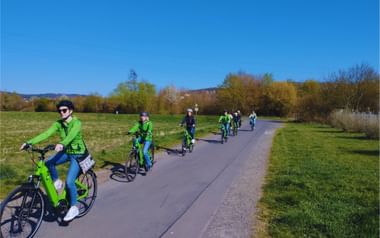 Gruppe von Radfahrern in leuchtend grüner Kleidung auf dem asphaltierten Lahnradweg durch grüne Landschaft bei Marburg unter blauem Himmel.